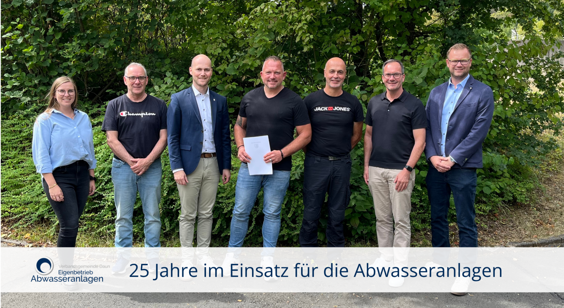 Sieben Personen vor grüner Hecke