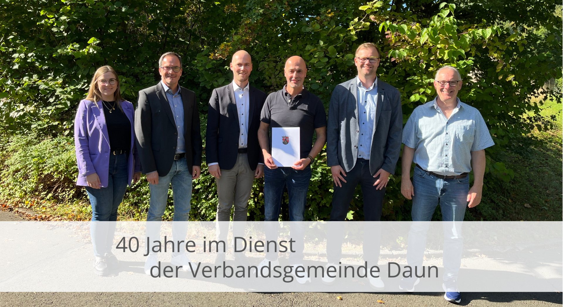 Personen mit dem Jubilar und einer Urkunde vor einer Hecke