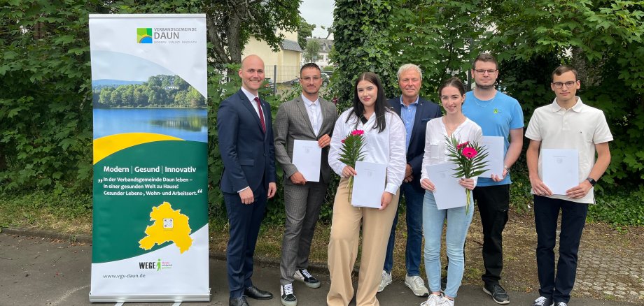 Personen zum Teil mit Urkunden vor Bäumen