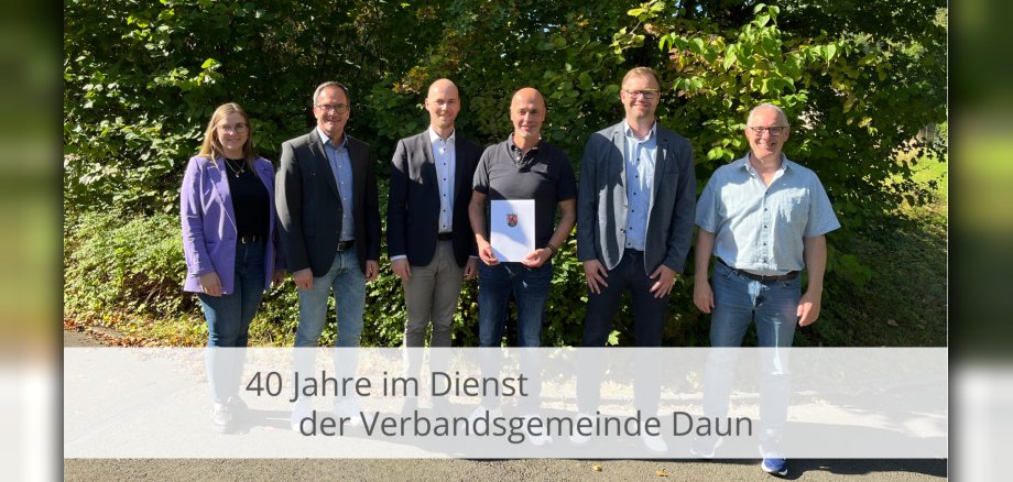 Personen mit dem Jubilar und einer Urkunde vor einer Hecke