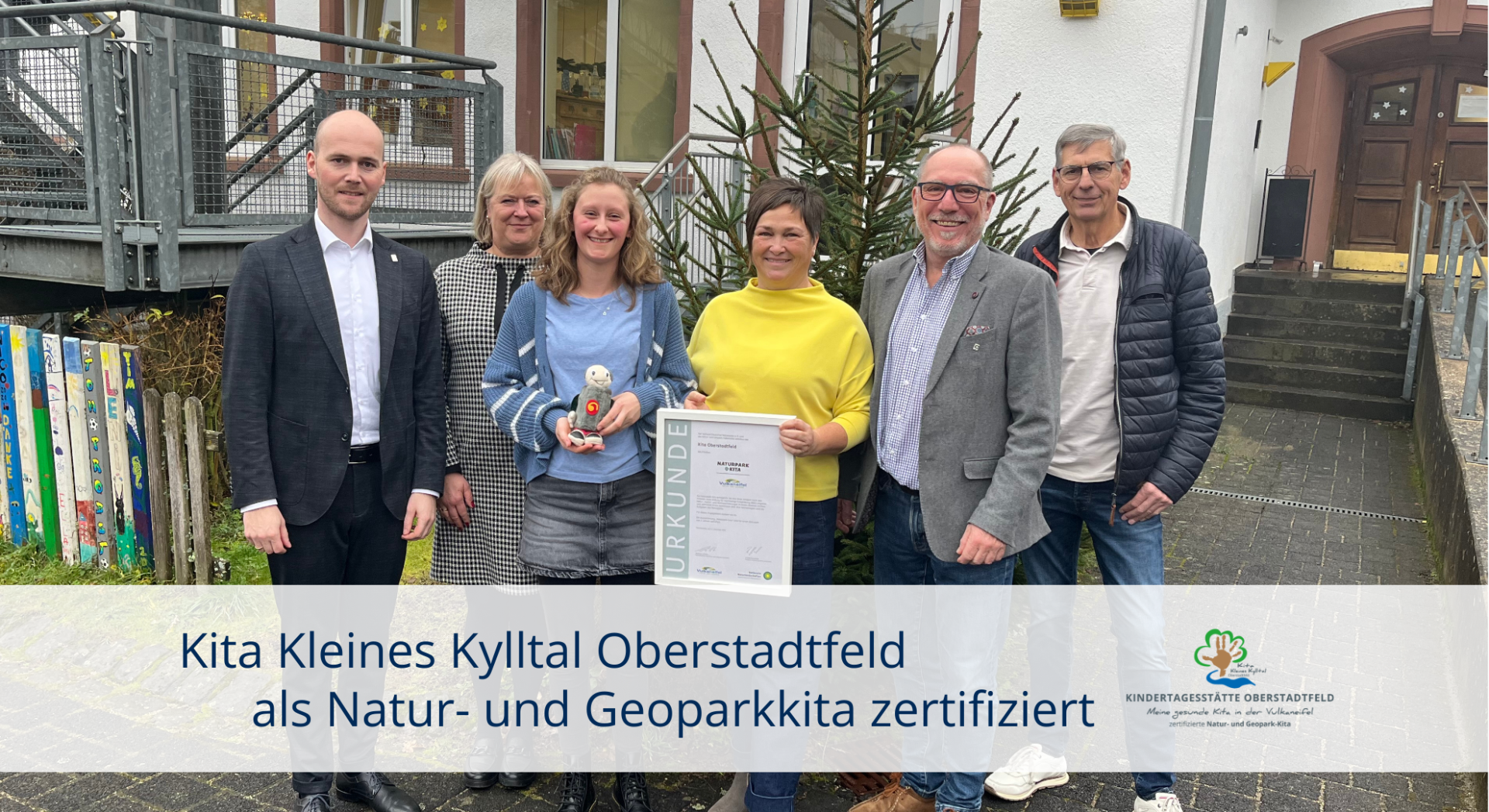 Sechs Personen mit Urkunde vor Kitagebäude